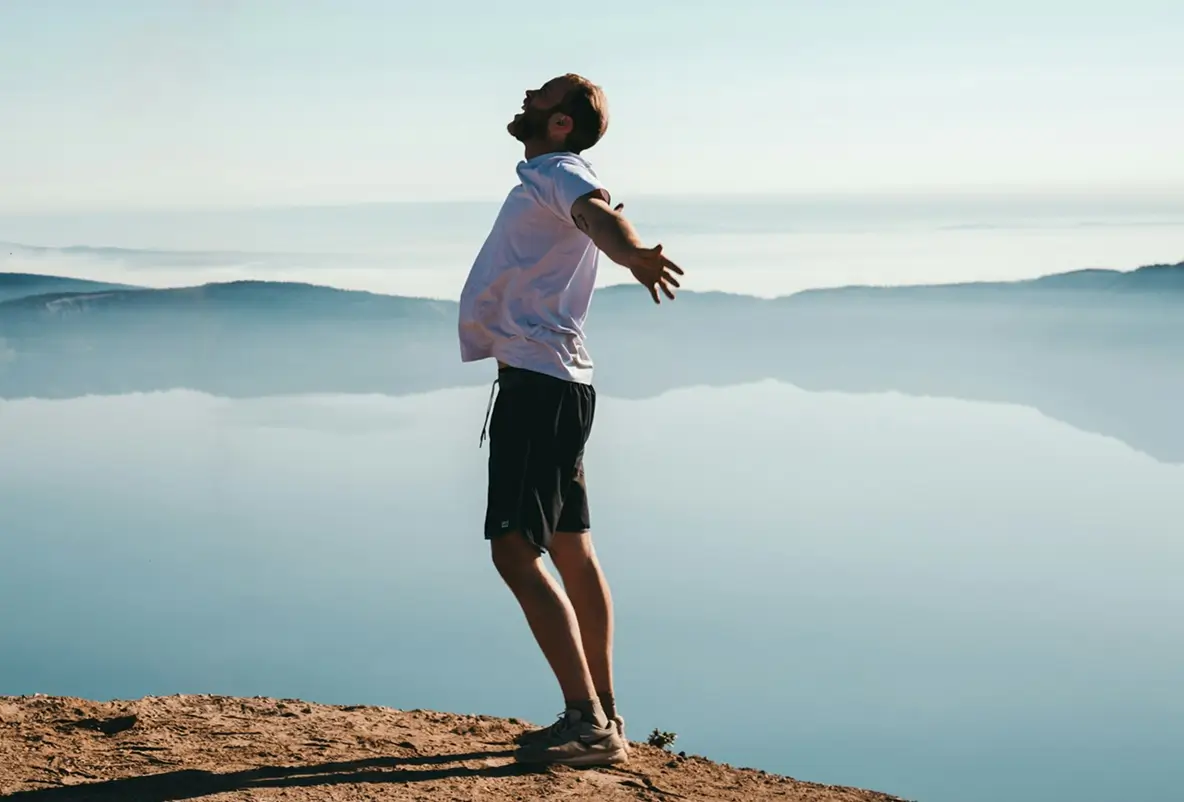 Person standing by a quiet lake with open space around them.